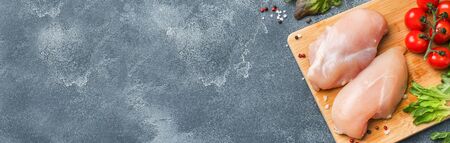 Raw chicken breast fillet with greens, tomatoes and spices on a dark background with copy spaceの写真素材