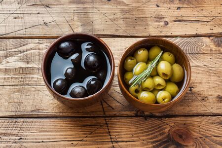 Black and green olives in wooden bowls on wooden table. Top view with space for textの写真素材