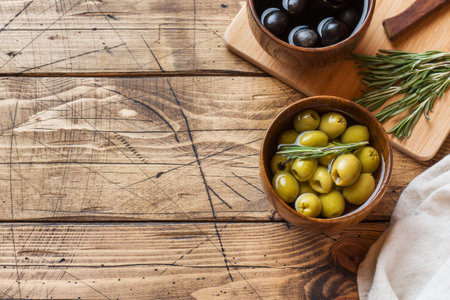 Black and green olives in wooden bowls on wooden table. Top view with space for text