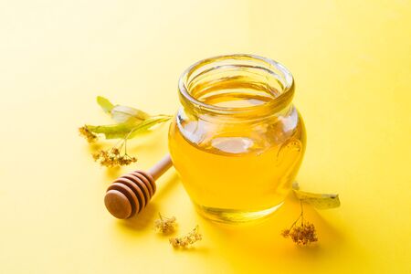 A jar of liquid honey from Linden flowers and a stick with honey on yellow background Copy spaceの写真素材