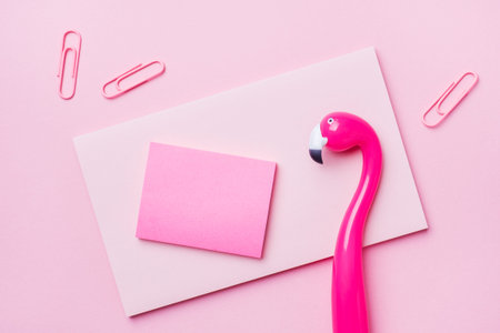 Pink Flamingo pen and writing pad on pink background. Copy space flat lay
