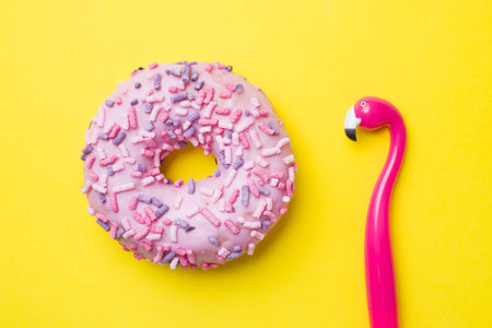 Pink doughnut and Flamingo pen on a yellow background. Top view Flat lay