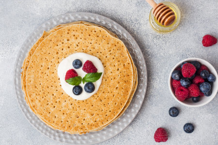 Plate of delicious thin pancakes with berries on grey table Copy space