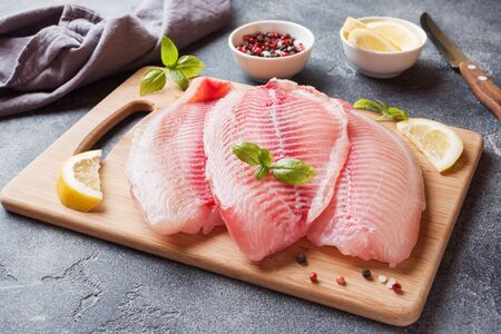 Raw fish fillet of tilapia on a cutting Board with lemon and spices. Dark table with copy spaceの写真素材