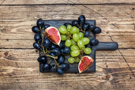 Clusters of black and green grapes Kish Mish and figs on a wooden Board. Copy spaceの写真素材
