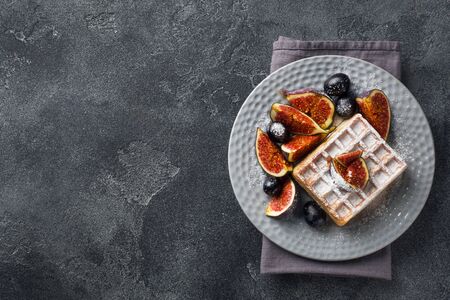 Traditional Belgian waffles with powdered sugar grapes and figs. Cozy homemade Breakfast. Gray concrete background. Copy spaceの写真素材
