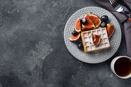 Traditional Belgian waffles with powdered sugar grapes and figs. Cozy homemade Breakfast. Gray concrete background. Copy spaceの写真素材