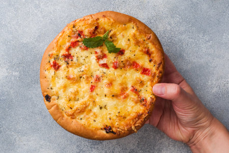 Homemade pizza tortilla with tomato and cheese on gray concrete background A woman's hand holding a...