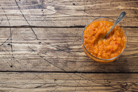 Homemade caviar from zucchini tomatoes and onions in a glass jar on a wooden background.