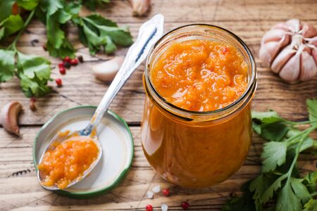 Homemade caviar from zucchini tomatoes and onions in a glass jar on a wooden background. Homemade production canning, canned stewed vegetableの写真素材