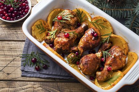 Baked chicken drumstick with oranges and cranberries in a baking sheet on a wooden background. Christmas food Table with decorationsの写真素材