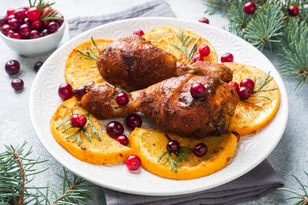 Baked chicken drumstick with oranges and cranberries in a plate light grey background. Christmas food Table with decorationsの写真素材