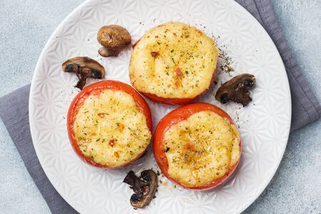 Baked whole tomatoes stuffed with mushrooms and cheese with spices on a light concrete backgroundの写真素材