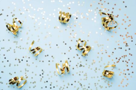 Flat lay background for celebration Christmas and New Year. gold ribbons bows and confetti stars on a blue background. top view copy spaceの写真素材