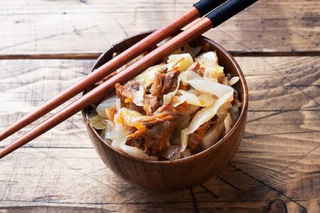 Stewed cabbage with meat in a wooden bowl on a wooden background. Traditional Russian dish of Solyankaの写真素材