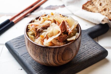 Stewed cabbage with meat in a wooden bowl on a wooden background. Traditional Russian dish of Solyankaの写真素材