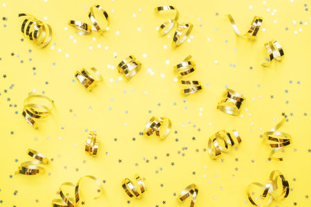 Gold confetti stars and ribbons on a yellow background. Copy space Flat lay. Greeting card for...