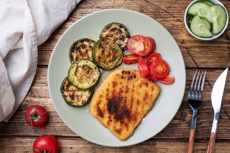 Schnitzel of chicken and zucchini cooked on the grill. Fresh tomatoes on a plate. Ready delicious dinner lunch Wooden backgroundの写真素材