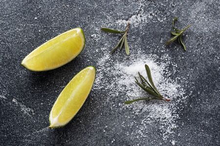 Slices of fresh lime, salt and rosemary dark concrete background. Copy space. Ingredients for making a tequila cocktailの写真素材