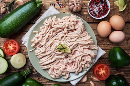 Raw minced chicken on a plate with spices on a Wooden background and raw vegetables zucchini tomato onion and eggs. Products to prepare the cutlets at homeの写真素材