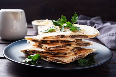 Pieces of quesadilla with mushrooms sour cream and cheese on a plate with parsley leaves. Wooden background close up.の写真素材