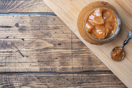 Boiled condensed milk with a glass jar on a wooden background. Sweet pasta spread for Breakfast and dessert. Copy spaceの写真素材