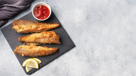 Fried fish hake Pollock with tomato sauce and slices of fresh lemon. Concept eating fatty fast food....