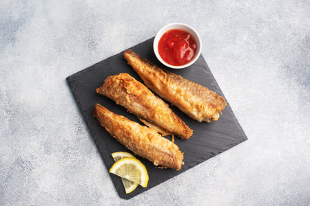Fried fish hake Pollock with tomato sauce and slices of fresh lemon. Concept eating fatty fast food....
