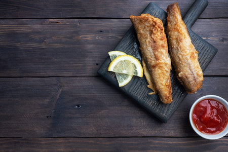 Fried fish hake Pollock with tomato sauce and slices of fresh lemon. Concept eating fatty fast food....
