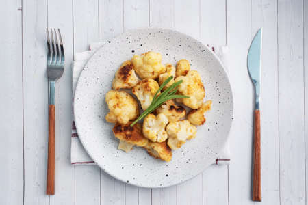 Fried cauliflower florets in batter on a white plate. White wooden background Copy space.の写真素材