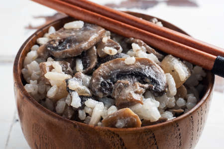Risotto with mushrooms in a wooden bowl and chopsticks. Boiled white rice with champignons in cream sauce. Light wooden background. Copy spaceの写真素材