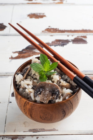 Risotto with mushrooms in a wooden bowl and chopsticks. Boiled white rice with champignons in cream sauce. Light wooden background. Copy spaceの写真素材