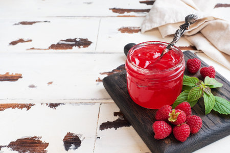 Homemade raspberry jam in a glass jar and fresh raspberries with mint on a wooden rustic background...
