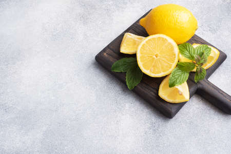 Juicy yellow lemons whole and cut with fresh mint leaves on a wooden stand. Copy spaceの写真素材