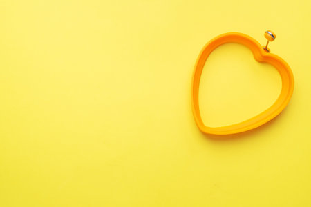 Heart shaped silicone mold for baking and frying eggs on a yellow background. Top view, minimalist, copy spaceの写真素材