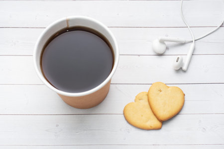 Black coffee in a paper cup and cookies in the shape of hearts on a white background. flat lay copy...
