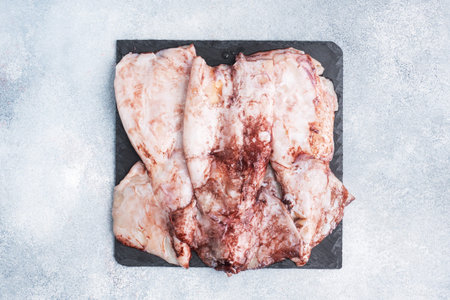 Raw squid carcass with spices on a black slate board. copy space Top view