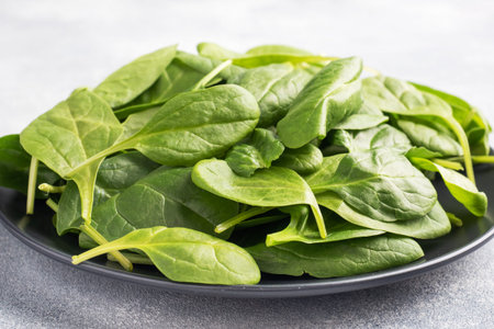 Spinach green fresh leaves on a black plate. Gray background, copy space