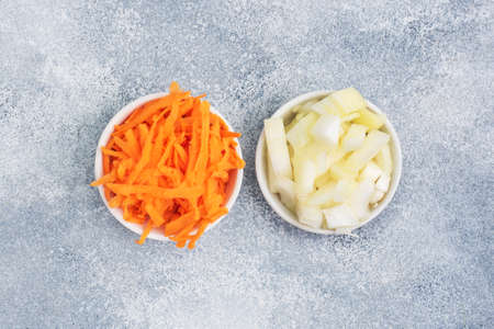 Grated carrots and chopped onions in a white plate. Raw vegetables, ingredients for roasting. gray background, copy space, top viewの写真素材