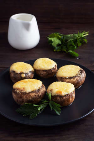 Baked mushrooms stuffed with cheese and herbs on a black plate. wooden backgroundの写真素材