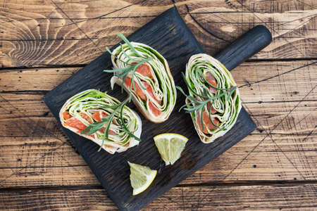 Rolls of thin pita bread and red salted salmon with lettuce leaves on a wooden cutting Board. Copy spaceの写真素材