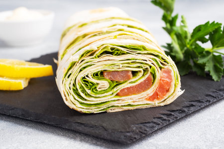 Rolls of thin pita bread and red salted salmon with lettuce leaves On a slate stand, gray concrete...