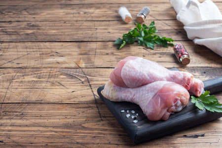 Raw chicken drumsticks with parsley and spices on a wooden cutting Board copy spaceの写真素材
