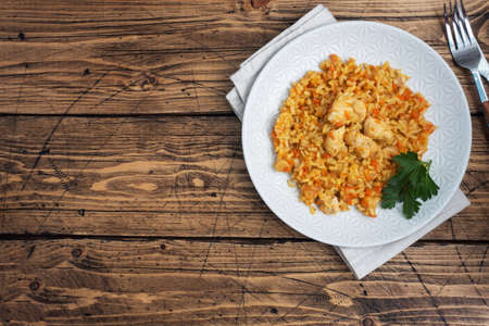 Delicious Asian pilaf, stewed rice with vegetables and chicken on a plate. Wooden rustic background copy space.の写真素材