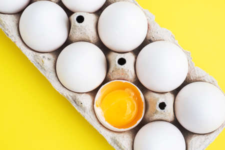Fresh chicken eggs in a package, raw eggs in a white shell in a box. Top view copy space, Yellow background. Broken egg with yolkの写真素材