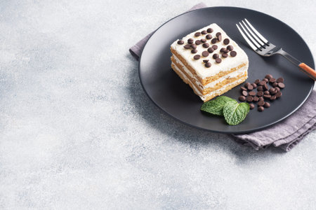 Sponge cake with buttercream and chocolate pieces mint on a black plate. Dessert for celebrate event...