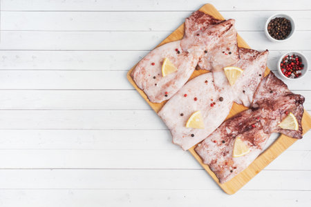 Raw squid carcass with spices and lemon ready for cooking on a wooden cutting board copy space. Top...