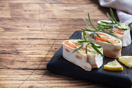 Rolls of thin pita bread and red salted salmon with lettuce leaves on a wooden cutting Board. Copy spaceの写真素材