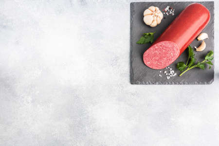 A loaf of salami Servelat sausage on a cutting Board with parsley and spices and garlic top view copy spaceの写真素材