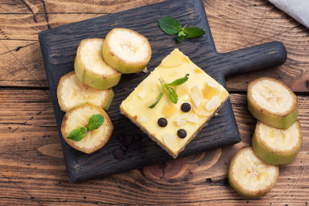 Banana sponge cake with nuts and chocolate drops. Delicious sweet dessert for tea, wooden background top view, copy space.の写真素材